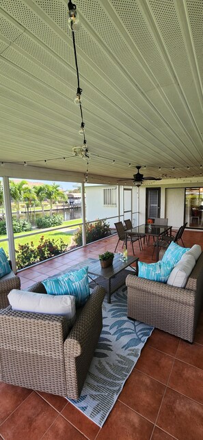 Ein überdachter Patio-Bereich mit Korbmöbeln, einem Esstisch und Stühlen.