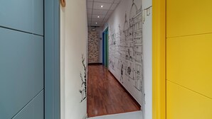 Un pasillo con piso de madera, paredes azules y amarillas, y un mural de dibujos arquitectónicos.