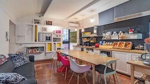 Una cocina moderna con encimeras de madera, un rincón de comedor con sillas coloridas y un sofá negro con cojines estampados.