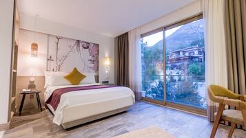 Une chambre d’hôtel moderne avec un grand lit, une table de chevet, une lampe, une chaise et une grande fenêtre donnant sur la montagne.