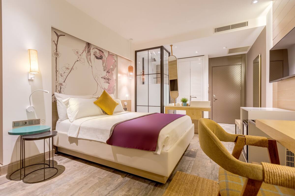 Una habitación de hotel moderna con cama, mesita de noche, lámpara, silla y un espejo grande.