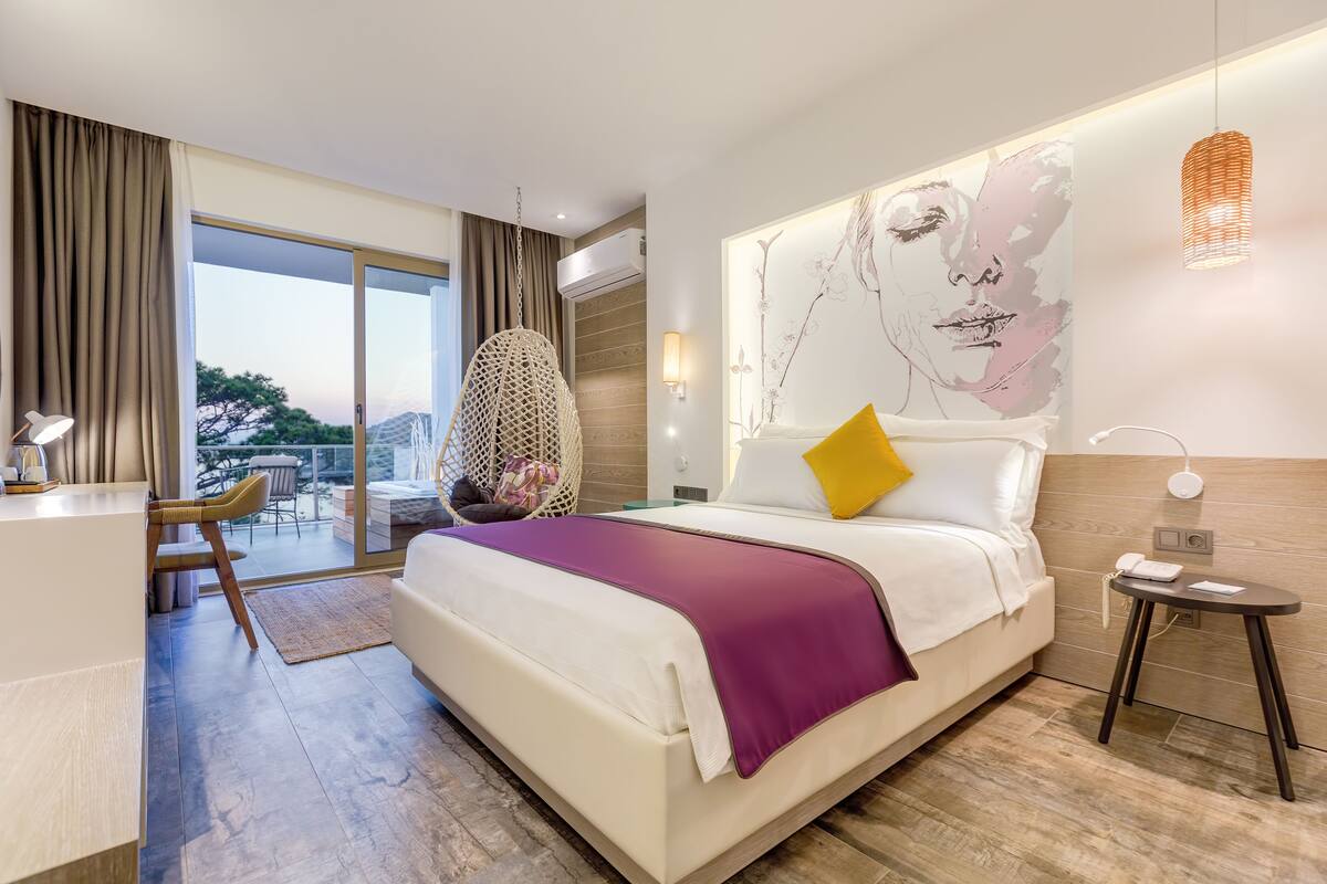 Una habitación de hotel moderna con una cama grande, un escritorio y un balcón con mobiliario exterior.