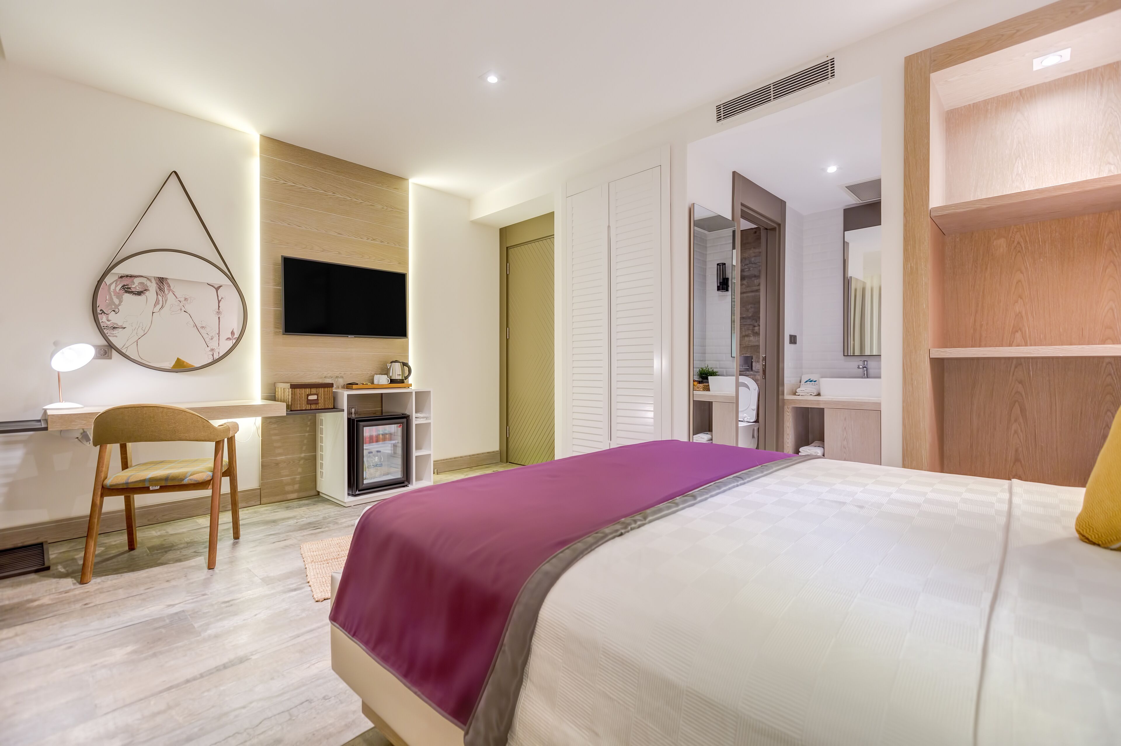 A modern hotel room with a bed, a desk, a chair, a television, and a bathroom.