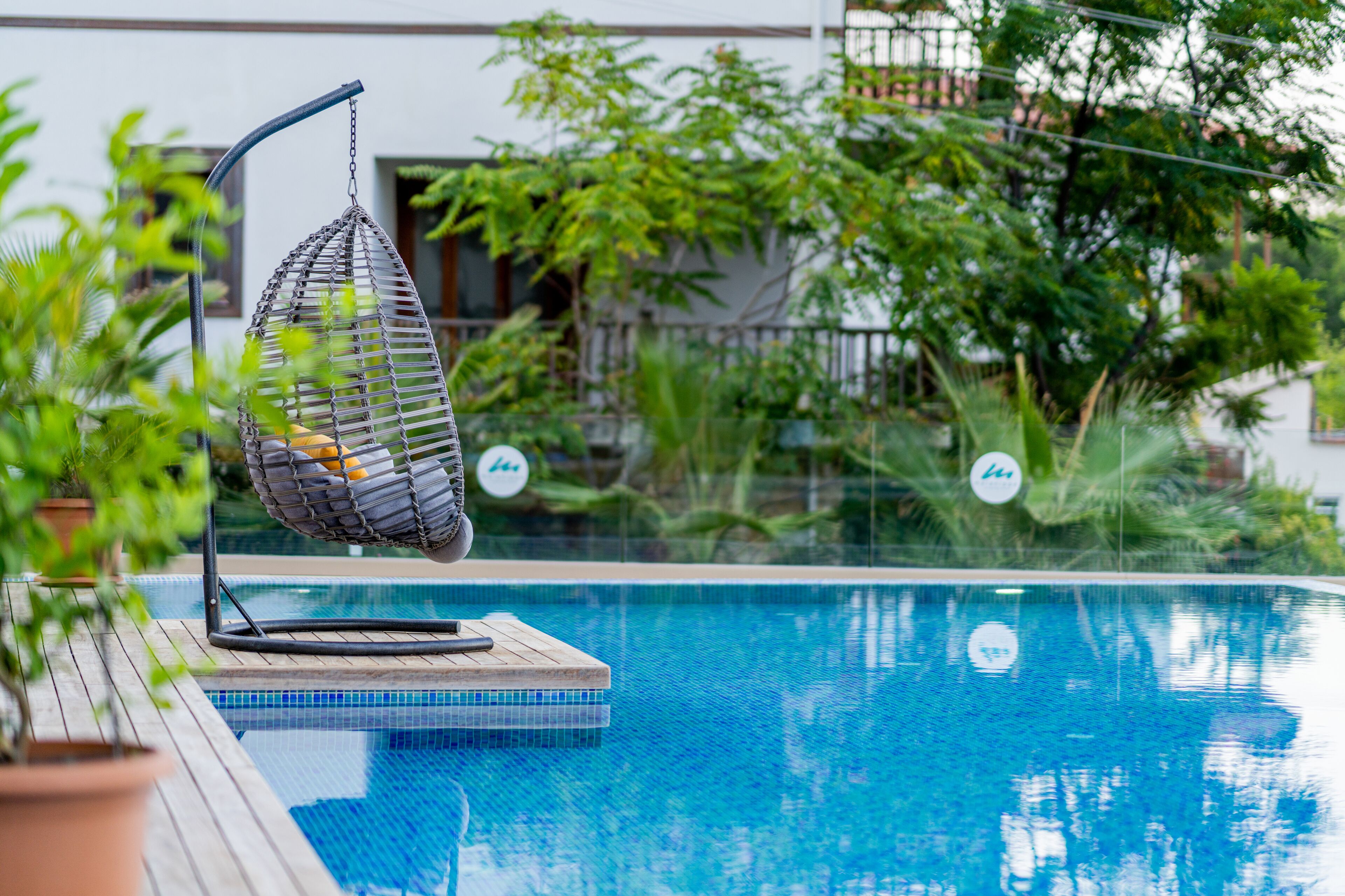 A pool area with a hanging chair, potted plants, and a wooden deck.
