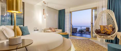 Una habitación de hotel moderna con una cama grande, una zona de estar con sofá y sillas, un balcón con vistas y una silla colgante.