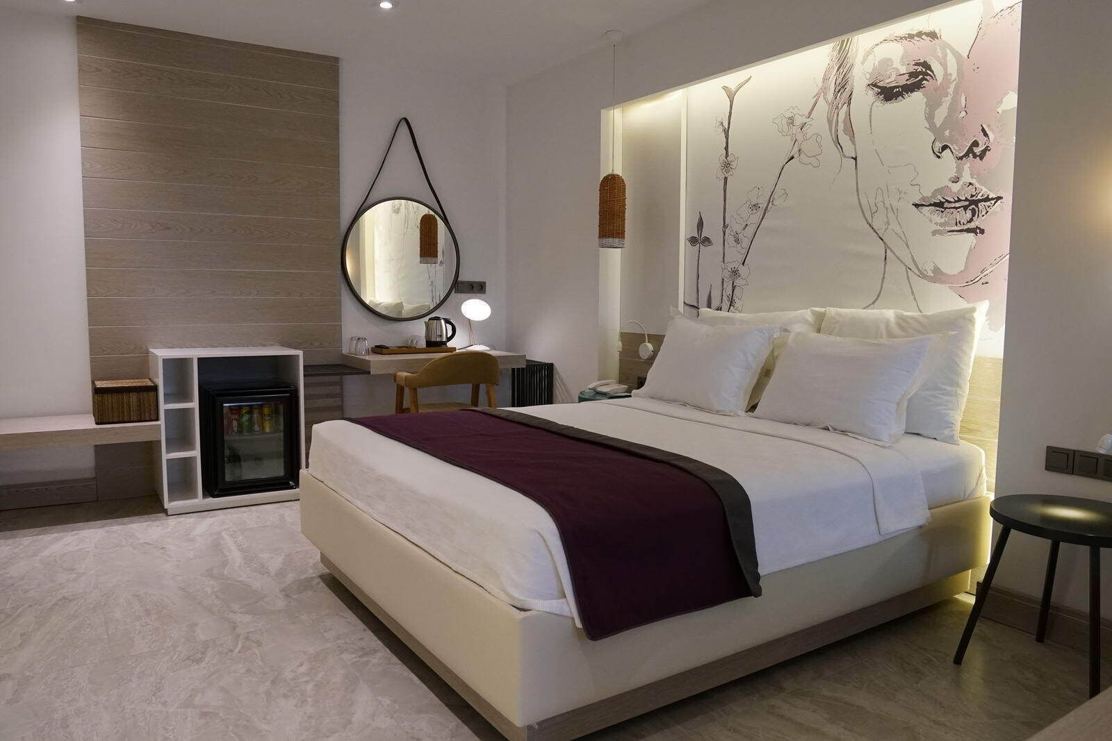 A modern bedroom with a large bed, a bedside table, a mirror, and a wall-mounted artwork.