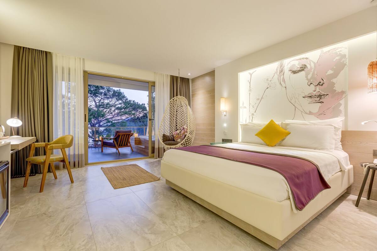 Una habitación de hotel moderna con una cama grande, un escritorio con silla y vistas al exterior.