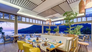 A restaurant with a terrace overlooking a scenic mountain view, featuring large windows, yellow chairs, and a modern ceiling design.