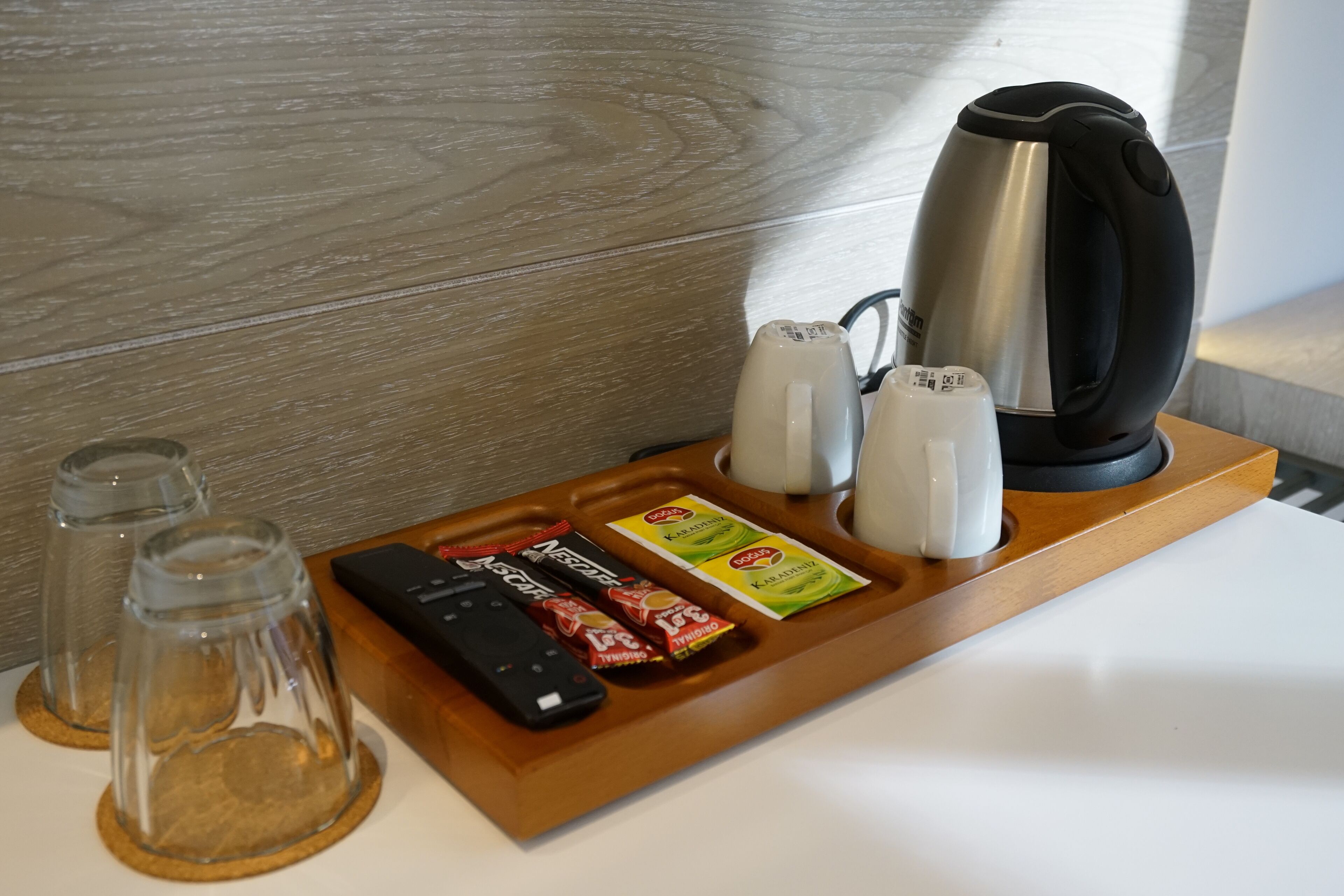 A tray with a kettle, two glass bottles, a remote control, and some snacks.