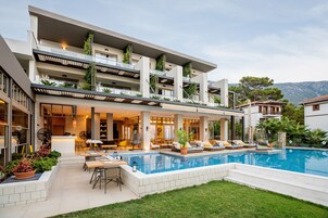 A modern multi-story building with a swimming pool, outdoor seating, and a view of the mountains.