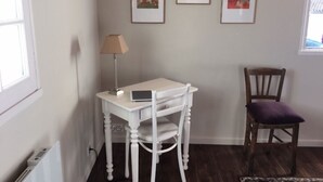 Een kamer met een witte tafel, een lamp, een stoel en drie afbeeldingen in lijsten aan de muur.