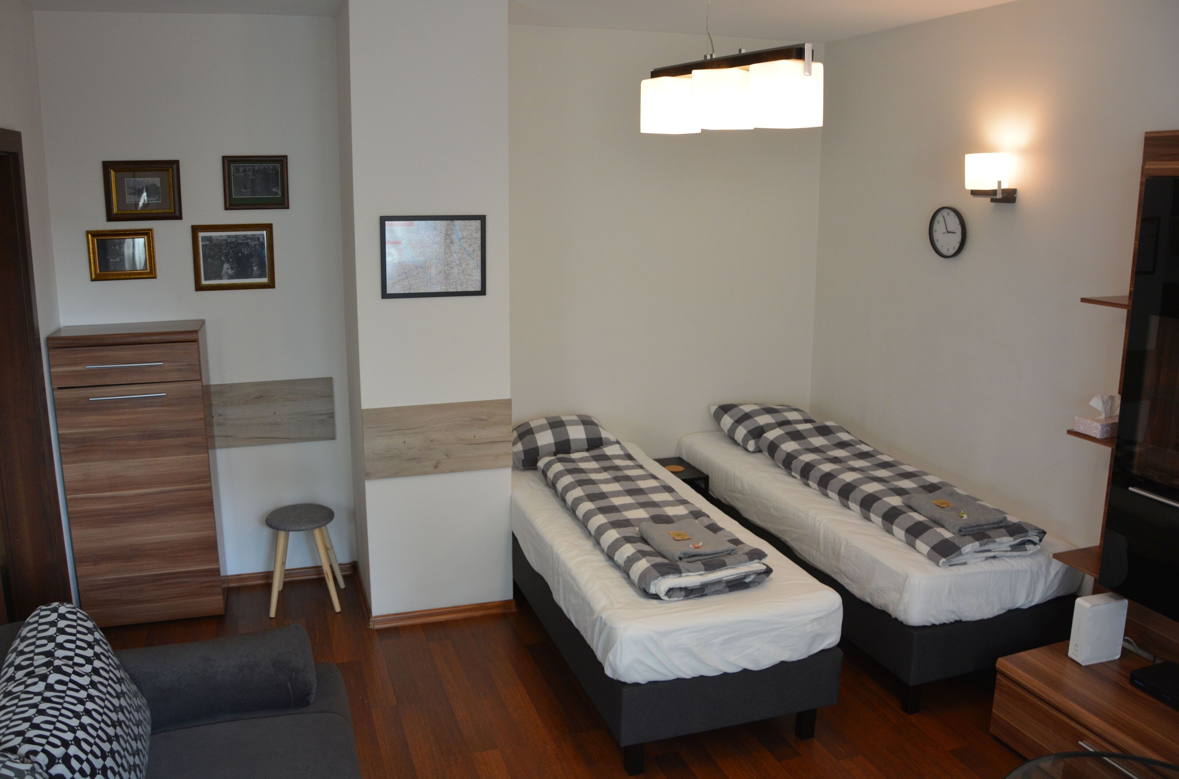 A modern bedroom with two single beds, a wooden dresser, a small stool, and a wall-mounted light fixture.