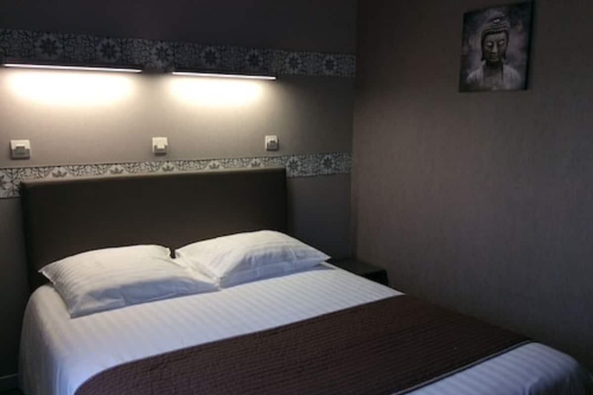 A neatly made bed with white linens and a brown throw blanket. There are two wall-mounted light fixtures above the bed.