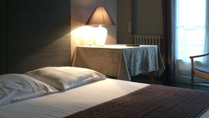 A hotel room with a bed, a bedside lamp, a small table with a tablecloth, and a chair. - Hotel le Berthelot (Tours)