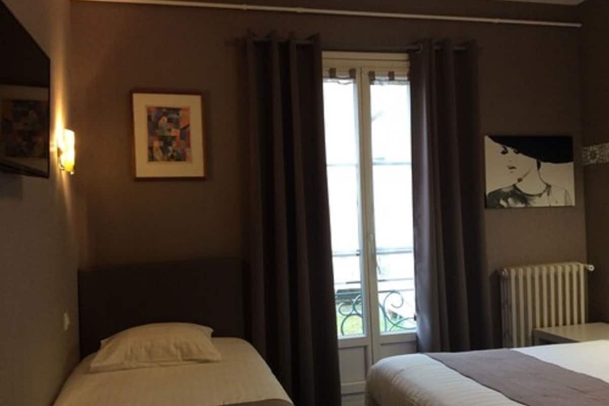 A hotel room with two beds, a window with curtains, a radiator, and artwork on the walls.