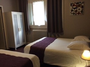 A hotel room with two beds, a wardrobe, a radiator, a window with curtains, and a wall-mounted artwork. - Hotel le Berthelot (Tours)
