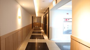 A hotel corridor with a checkered floor pattern, wooden paneling on the walls, and a door with a red emergency button. - I Hotel&Motel (Pyeongtaek)