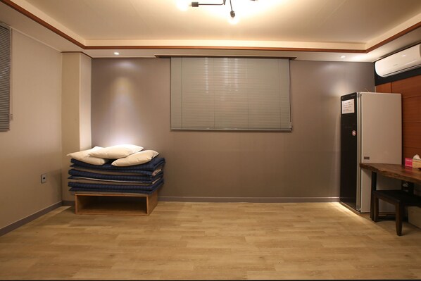 Una habitación pequeña con cama, una mesita y aire acondicionado integrado.