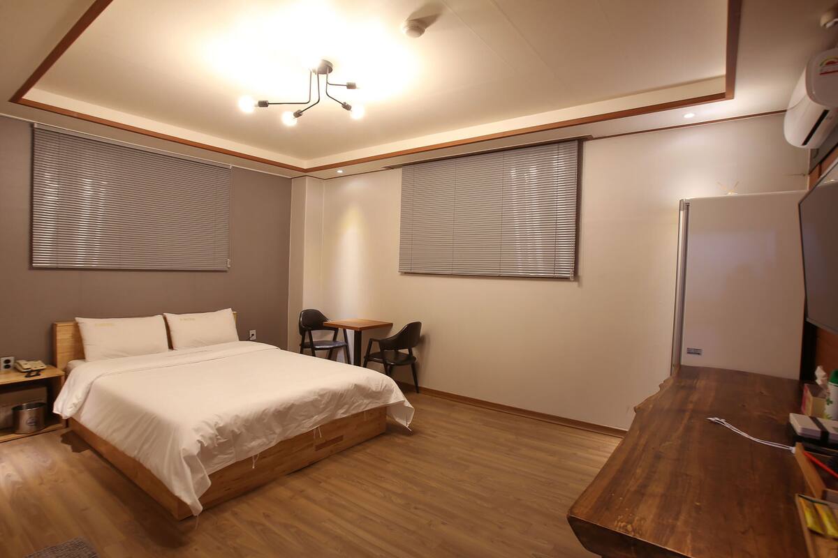 A bedroom with a wooden bed, a desk, two chairs, and a small table.