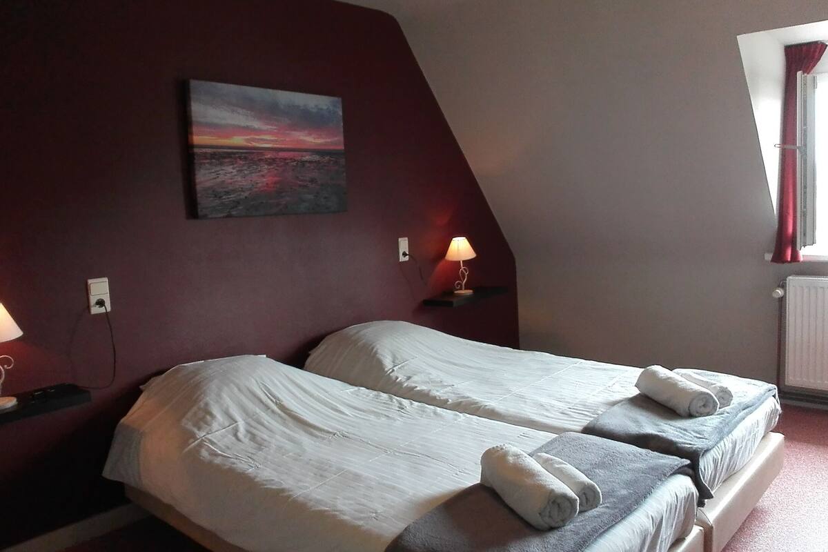 A bedroom with two beds, a painting on the wall, and two bedside lamps.