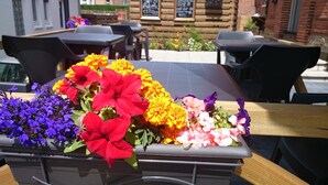 Un arreglo floral sobre una mesa frente a un edificio con paredes de ladrillo y mobiliario exterior.