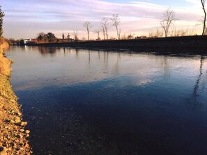 Un río tranquilo con un terraplén de piedra a un lado y un cielo despejado arriba.