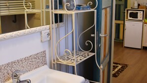 Un baño con un lavamanos blanco, un espejo y un estante metálico.