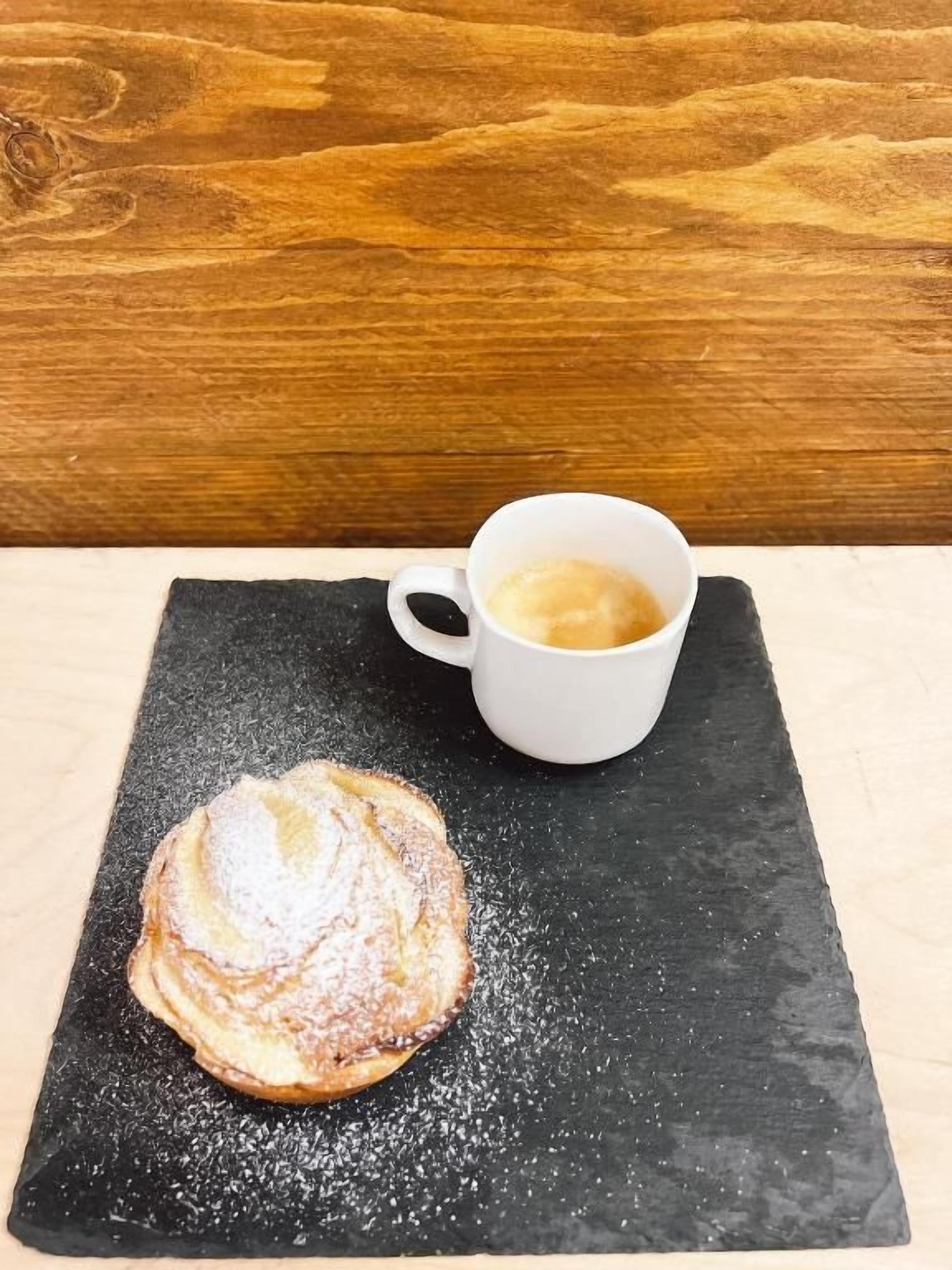 Un pastel sobre un plato de pizarra negra con una taza de café a su lado.