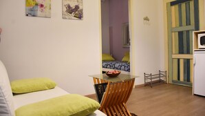 Una habitación pequeña con una cama, una mesa con un cuenco, un espejo y una puerta que da a otra habitación.