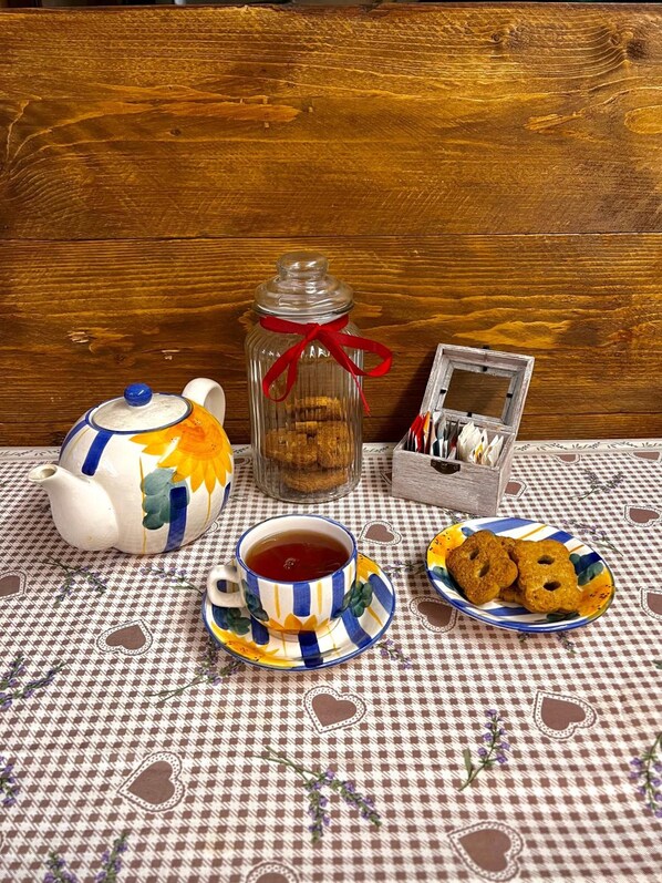 Una mesa con tetera, taza, galletas y una pequeña caja de cubiertos sobre un mantel a cuadros.