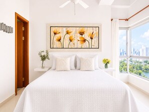 Un dormitorio con cama, vista a la ciudad, ventilador de techo y un cuadro de flores.