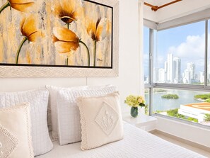 A modern bedroom with a large window, a city view, and a framed painting.