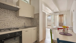 A modern kitchen with a gas stove, oven, and patterned backsplash. There is a dining area with a table, chairs, and a vase with flowers. - Tenuta Fioravante (Porto Cesareo)