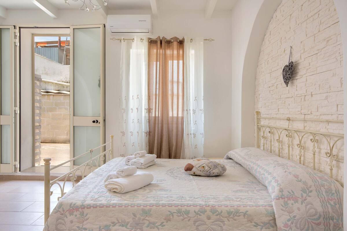 Een slaapkamer met een bed, een wandlamp en uitzicht door een open deur.
