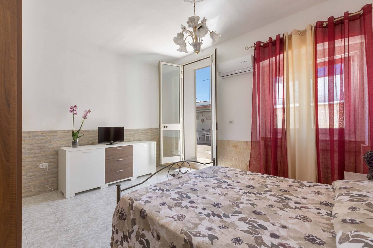 Een slaapkamer met een bed, een televisie, een dressoir en een spiegel.