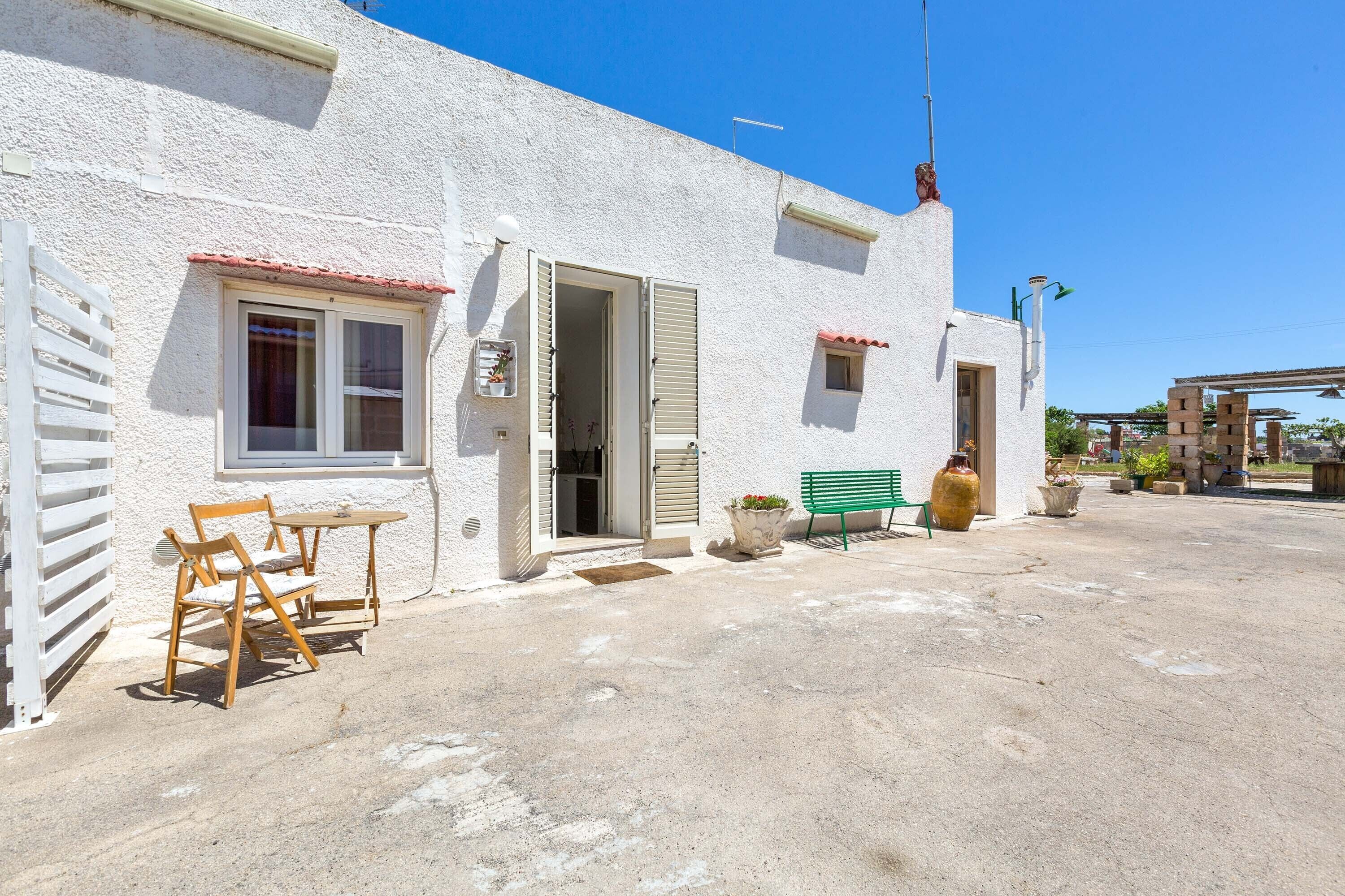 Un bâtiment blanc avec un toit recouvert de tuiles rouges, une table et des chaises en bois à l’extérieur, et un banc vert.