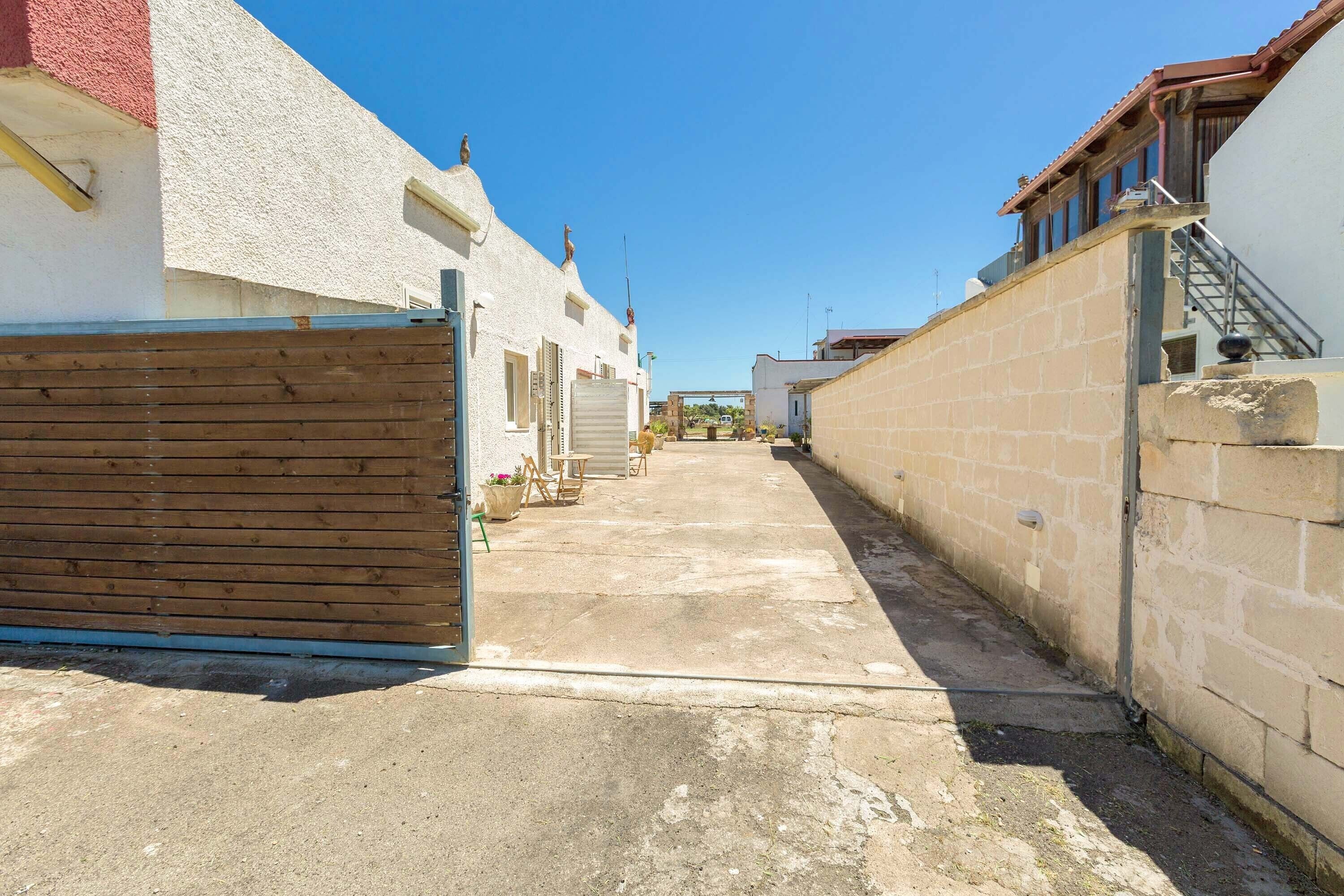 Um beco estreito entre edifícios, com um portão de madeira, uma parede de pedra e um céu azul claro.
