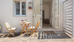 An outdoor seating area with two wooden chairs and a table, a window with shutters, and a door leading inside. - Tenuta Fioravante (Porto Cesareo)