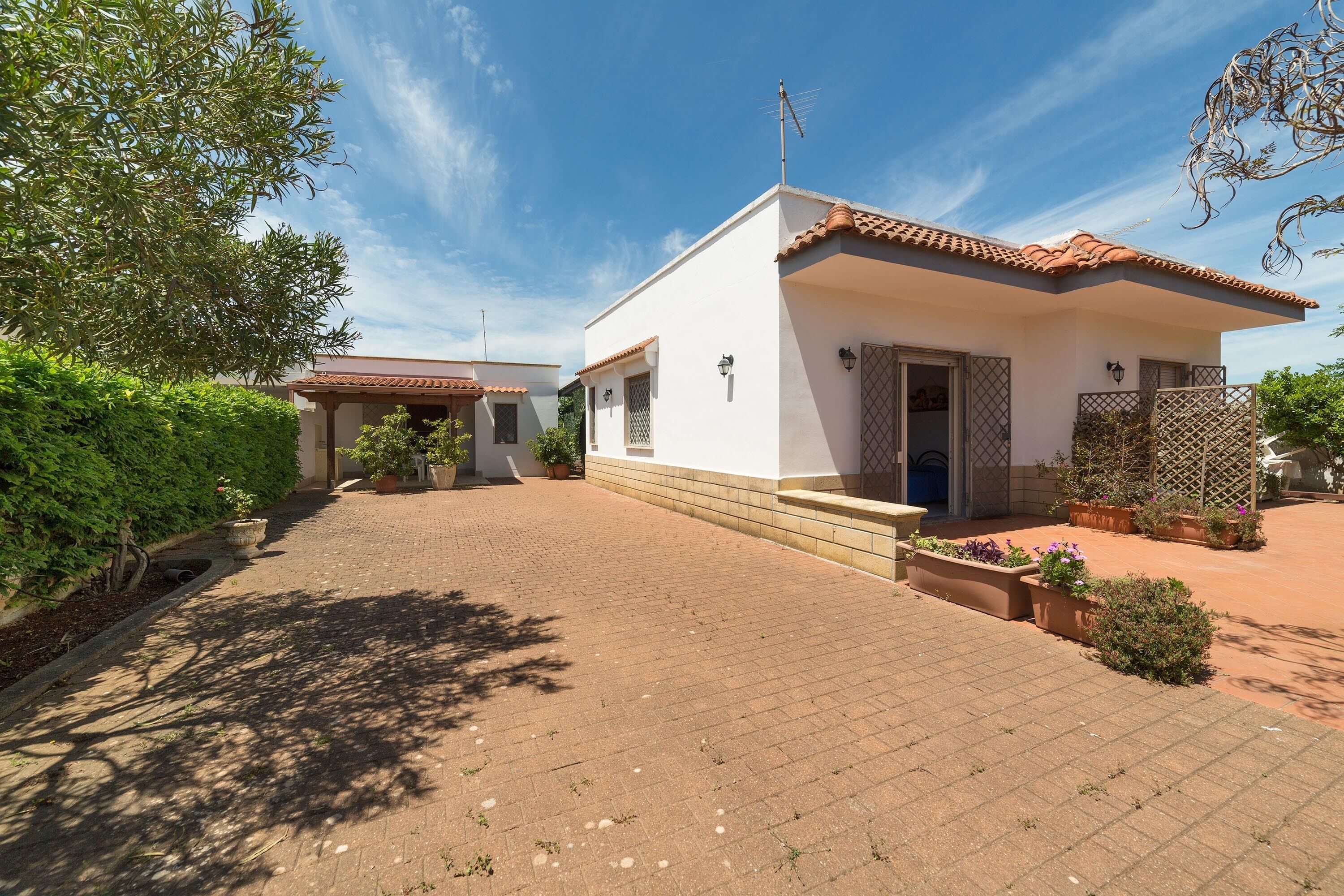 Una casa de dos pisos con techo de tejas, camino de entrada pavimentado y un jardín con plantas en macetas.