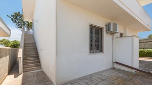 A residential building with a staircase leading to a door, a window with bars, and an air conditioning unit mounted on the wall. - Villa Spiaggia degli Angeli (Porto Cesareo)