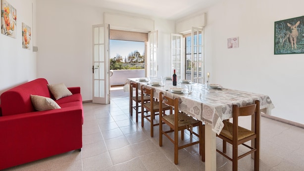 A dining area with a red sofa, a table set for four, and a view through an open door. - Villa Spiaggia degli Angeli (Porto Cesareo)