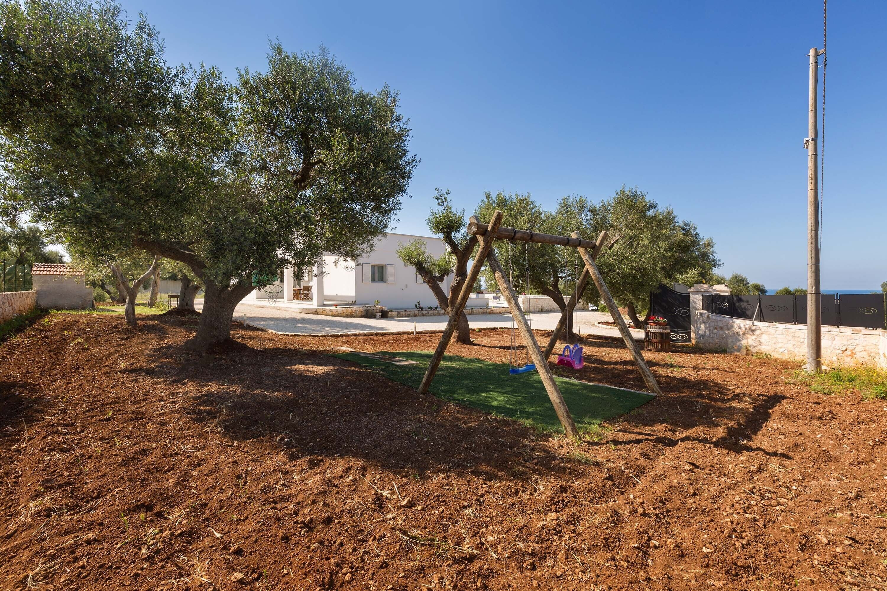 A playground with a swing set and a dirt area, surrounded by trees and a white building.