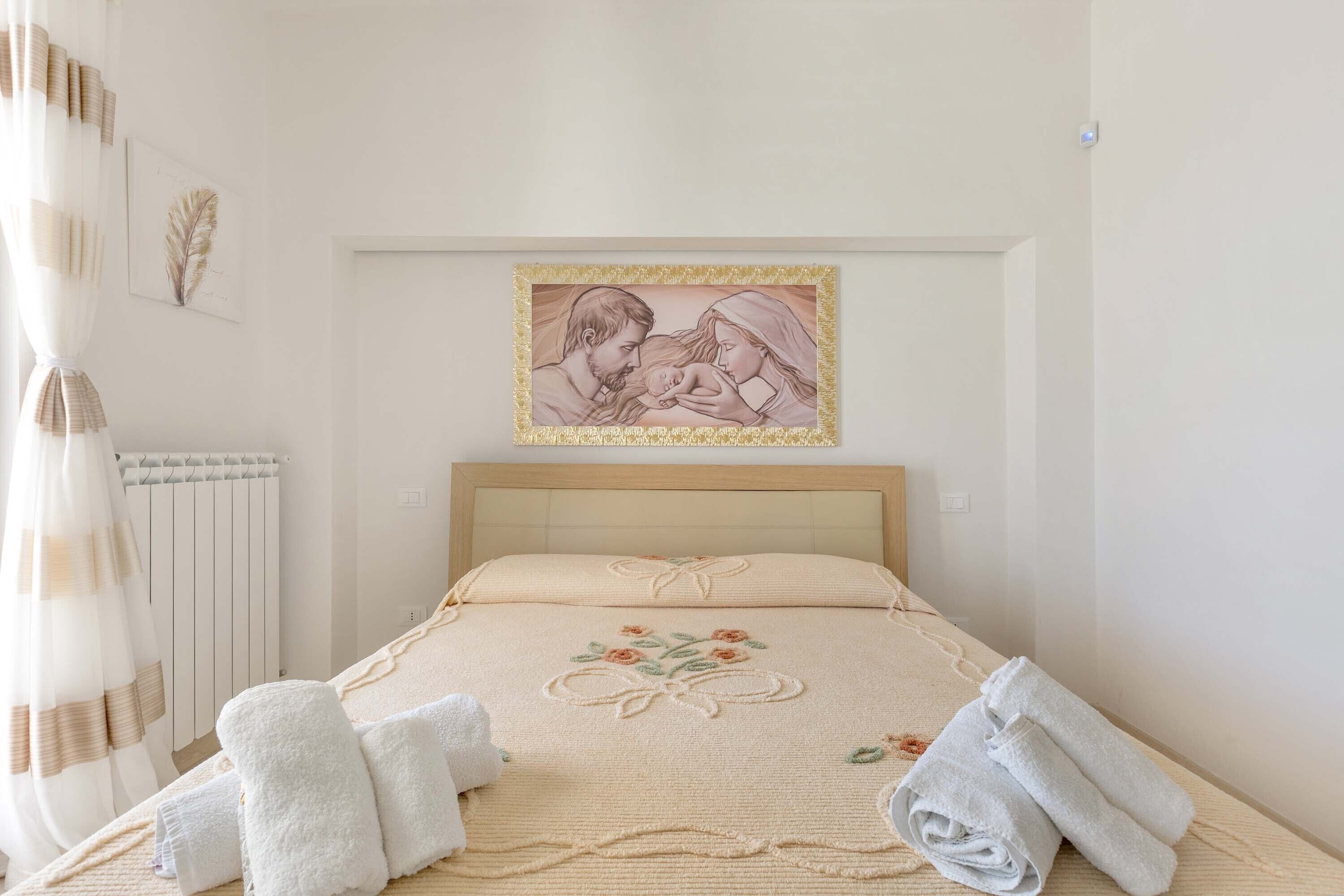 A bedroom with a bed, a framed picture on the wall, and towels on the bed.