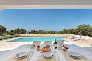 Un espace de restauration en plein air avec vue sur la piscine, des tables dressées avec des assiettes, des verres et une bouteille de vin.