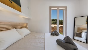 Un dormitorio con cama, ventana con vista a árboles y espejo.