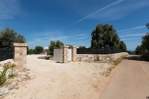 A gravel driveway leading to a gated entrance with stone walls and a metal gate. - Villa Orizzonte (Carovigno)