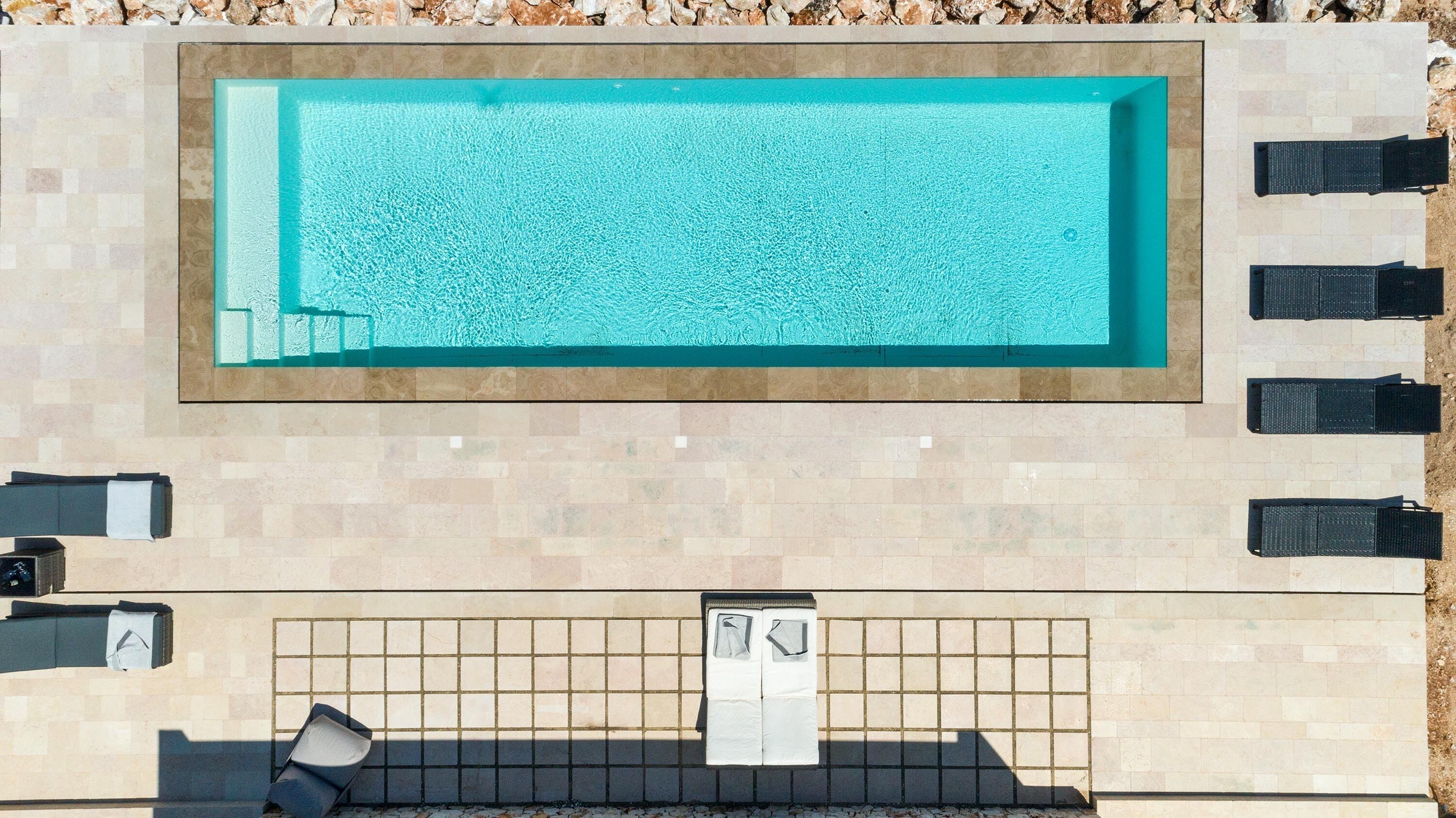 An outdoor swimming pool with a tiled deck, lounge chairs, and a sunshade.