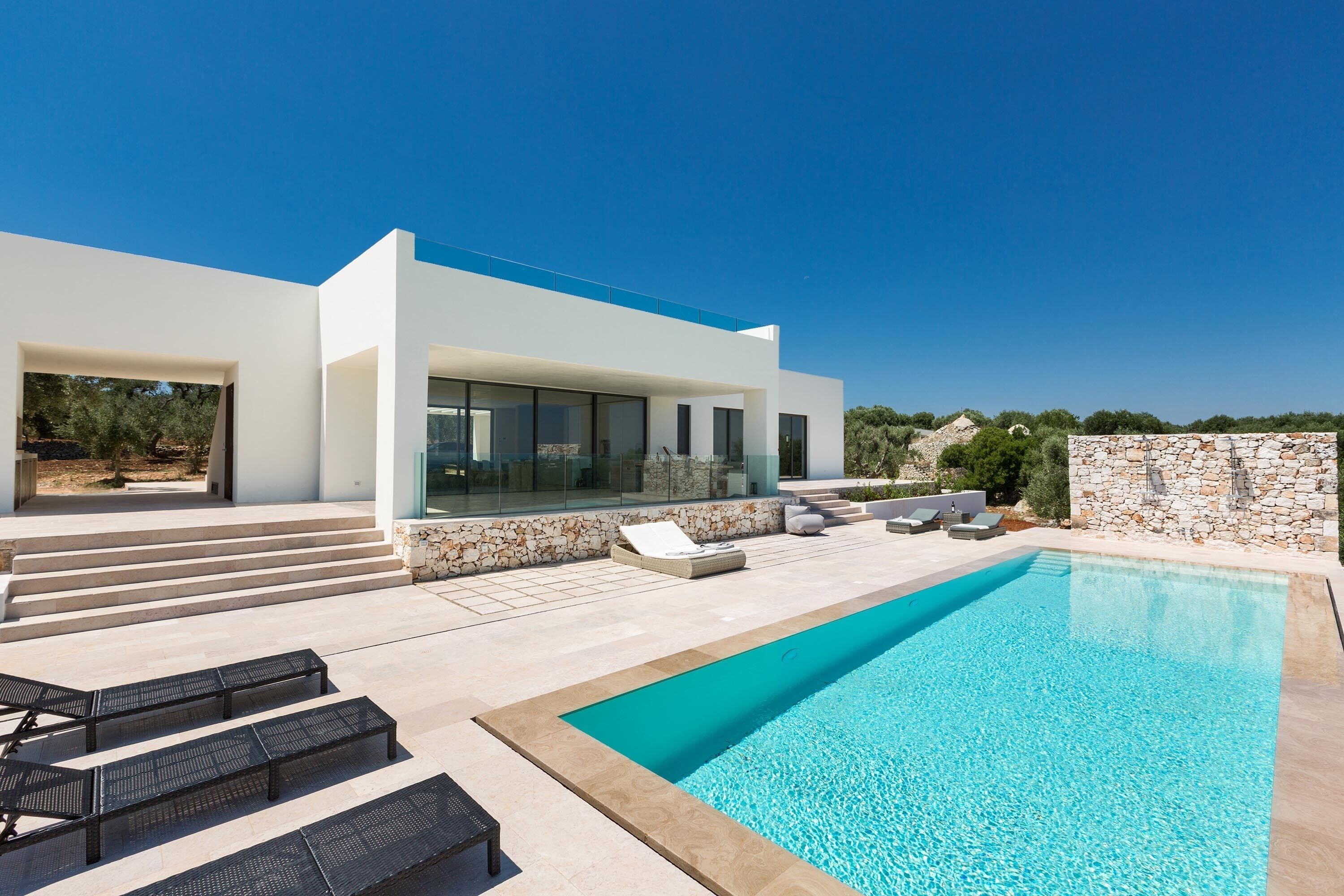 A modern house with a swimming pool, outdoor seating, and a stone wall.