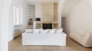 Een moderne woonkamer met een open haard, witte banken en een accentmuur van steen.