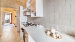 A modern kitchen with white cabinetry, a gas stove, and a countertop with kitchenware. - Casetta Annarosa (San Pancrazio Salentino)